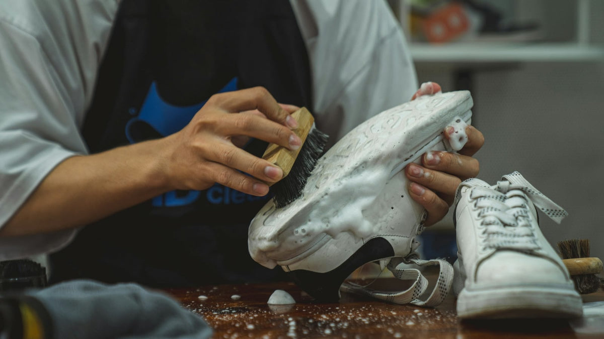 Someone scrubbing a white sneaker with foam and a cleaning brush