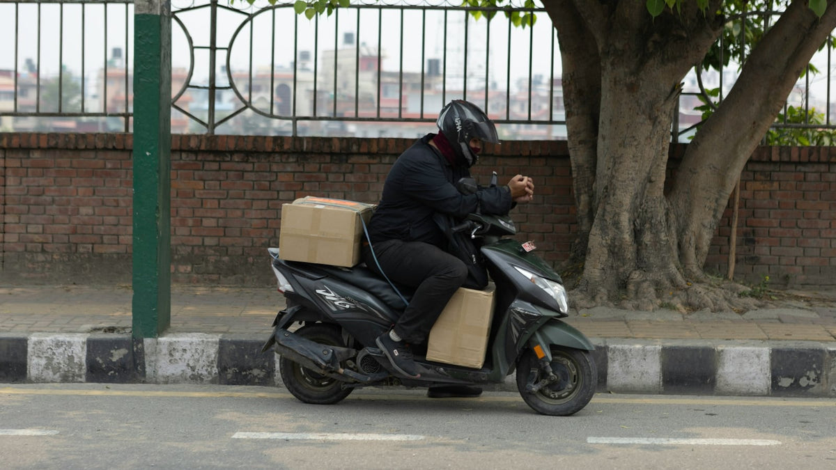 A delivery rider carrying cardboard parcels on the back of a scooter