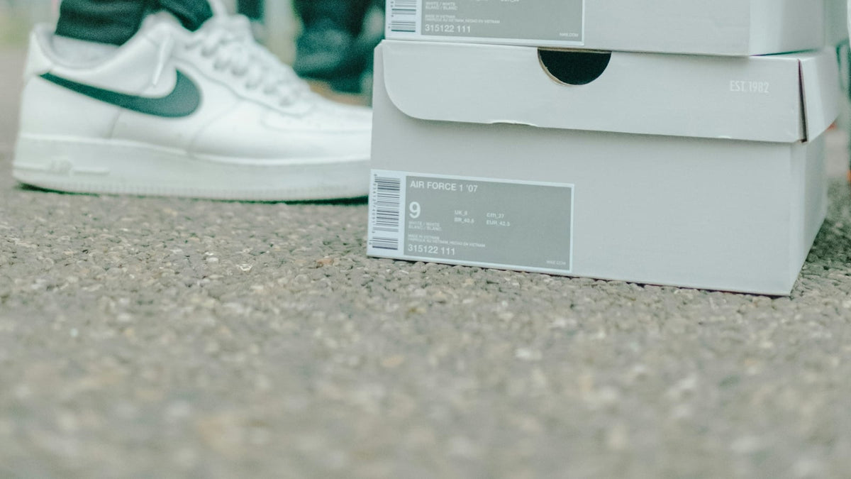 Stacked Nike Air Force 1 shoe boxes with the size label reading 9, next to a worn white pair